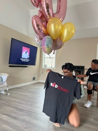 a woman holding up a t - shirt with balloons