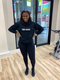 a woman standing in a gym wearing a black hoodie