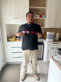 a man in a black t - shirt standing in a kitchen